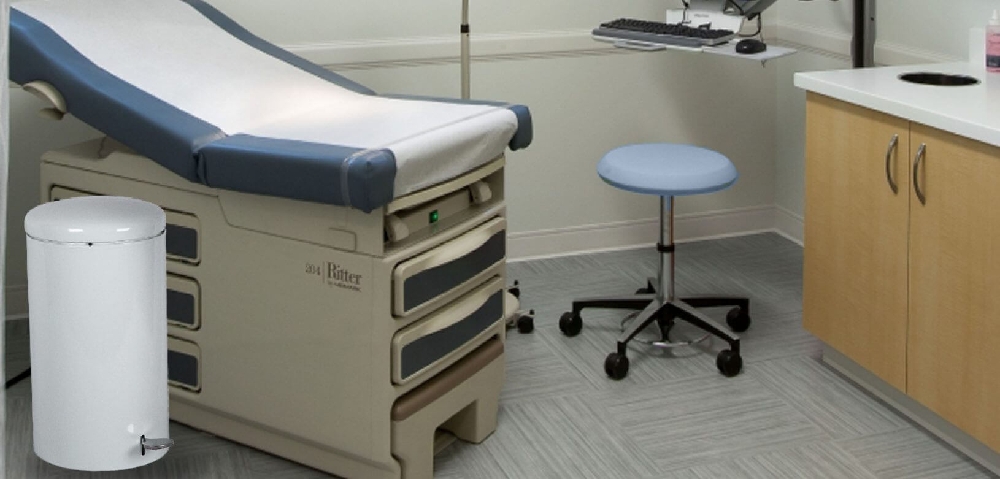 White step-on indoor trash can positioned in a medical exam room for hands-free, sanitary waste disposal.